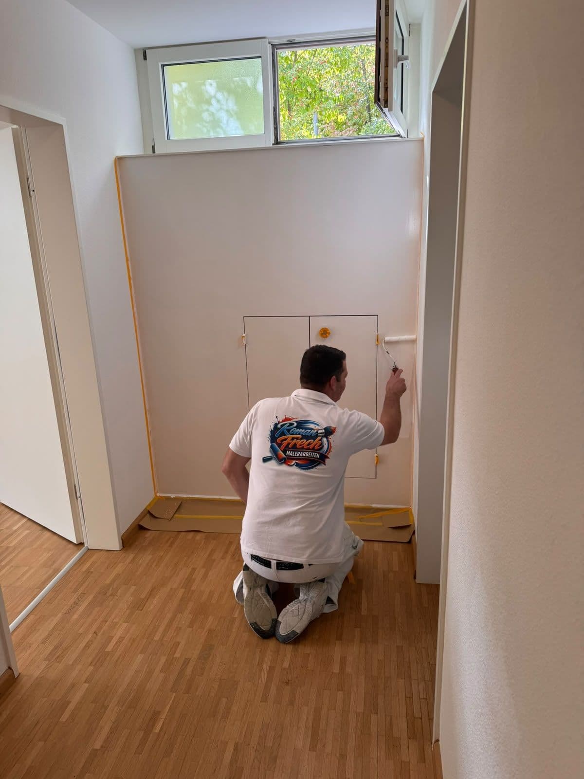 Roman Frech streicht im Flur einer Wohnung eine Wand mit eingebautem Wandschrank, Boden abgedeckt