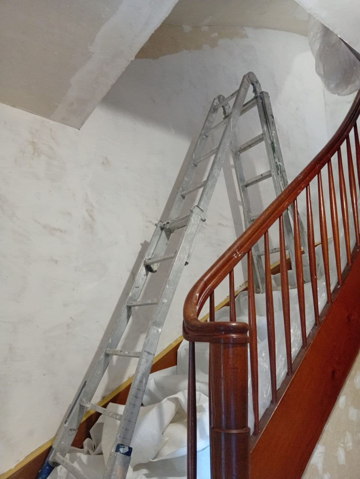 Treppenhaus während der Renovation mit Holzgeländer und frisch verputzten Wänden